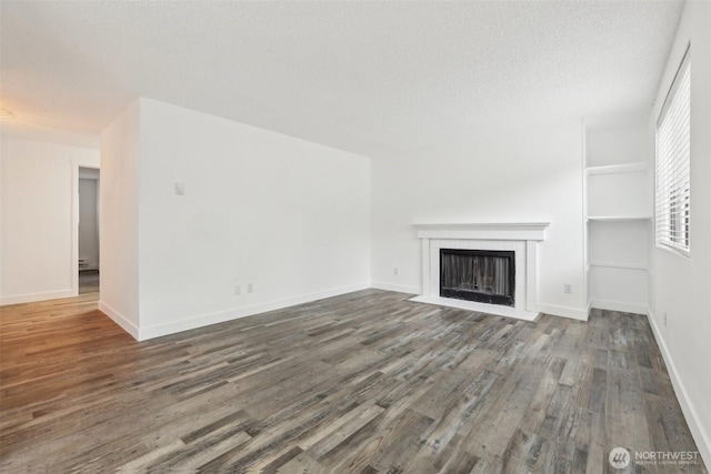 unfurnished living room featuring a tile fireplace, wood finished floors, baseboards, and a textured ceiling