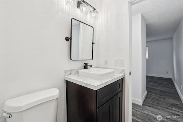 bathroom with toilet, vanity, wood finished floors, and baseboards
