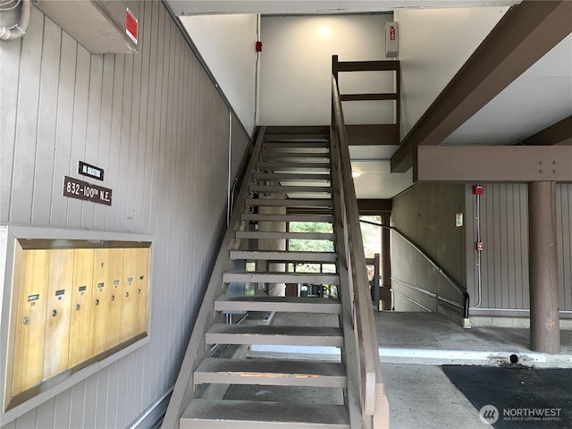 stairway with wooden walls, mail area, and concrete floors