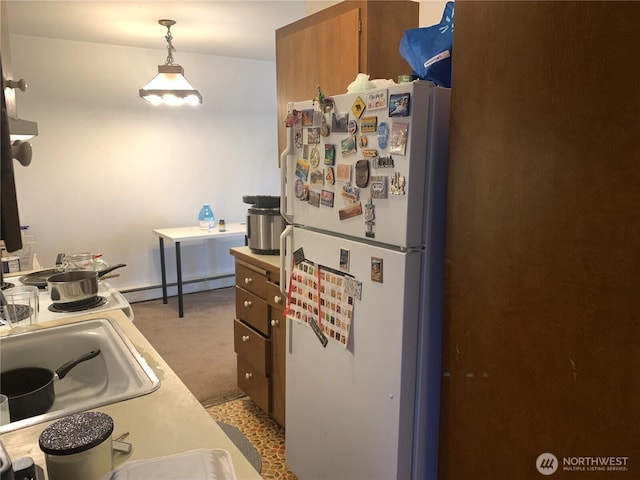 kitchen featuring freestanding refrigerator, a baseboard heating unit, light colored carpet, a sink, and brown cabinets