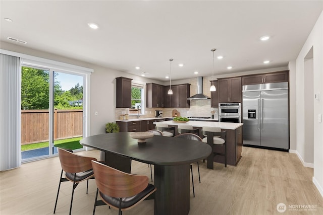 13436 NE 105th Ct Unit 17, Kirkland, WA 98033 - kitchen with appliances with stainless steel finishes, wall chimney exhaust hood, dark brown cabinets, light wood-type flooring, and backsplash
