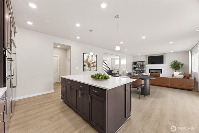 13436 NE 105th Ct Unit 17, Kirkland, WA 98033 - kitchen featuring light wood finished floors, dark brown cabinetry, light countertops, a glass covered fireplace, and baseboards