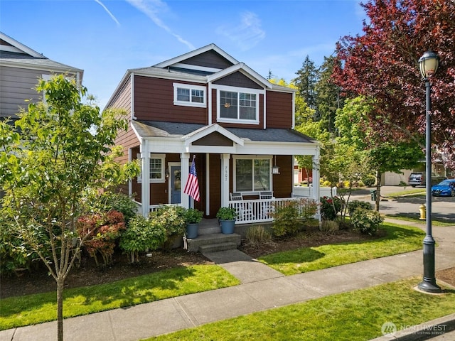 view of front facade with a porch, a front lawn, and a shingled roof