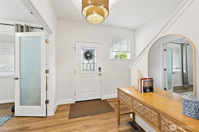 entrance foyer featuring light wood finished floors, a chandelier, baseboards, and arched walkways