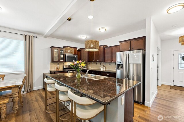 kitchen featuring appliances with stainless steel finishes, a sink, backsplash, dark brown cabinets, and wood finished floors