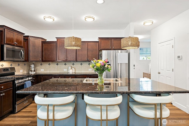 kitchen featuring stainless steel appliances, wood finished floors, dark brown cabinetry, and backsplash