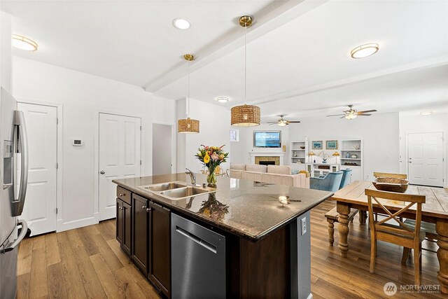 kitchen featuring a sink, appliances with stainless steel finishes, wood finished floors, a tile fireplace, and decorative light fixtures