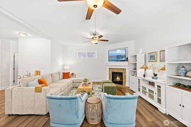 living room featuring a ceiling fan, wood finished floors, a tiled fireplace, and baseboards