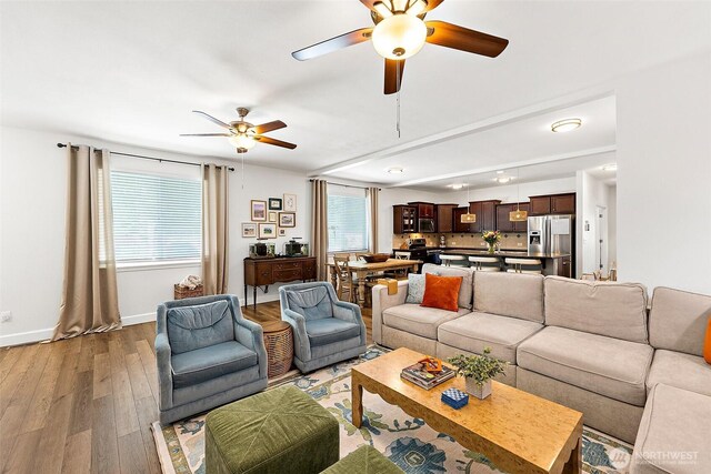 living area featuring a ceiling fan, light wood-style floors, healthy amount of natural light, and baseboards