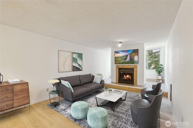 living room with wood finished floors, a textured ceiling, a tiled fireplace, and baseboards