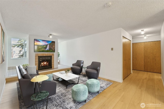 living area with a tile fireplace, light wood-type flooring, and a textured ceiling