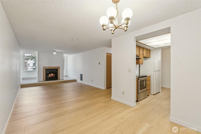 unfurnished living room featuring light wood-style floors, a textured ceiling, a chandelier, a tile fireplace, and baseboards