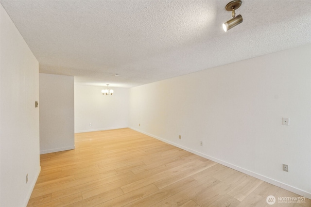 spare room with light wood finished floors, a textured ceiling, a chandelier, and baseboards