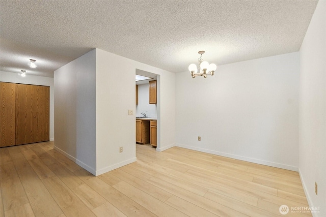 spare room with a chandelier, light wood-style flooring, a textured ceiling, and baseboards