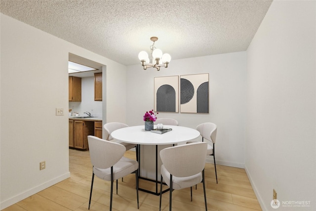 dining room with a chandelier, light wood-style floors, baseboards, and a textured ceiling