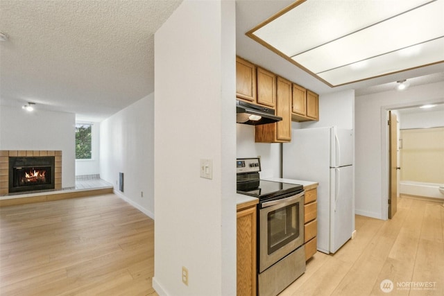 kitchen featuring electric range, under cabinet range hood, light wood finished floors, light countertops, and a tiled fireplace
