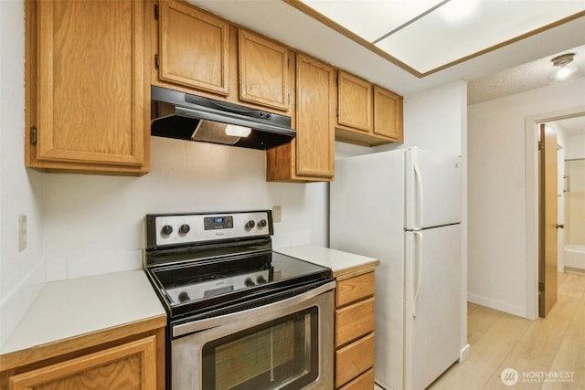 kitchen featuring electric stove, under cabinet range hood, freestanding refrigerator, and light countertops