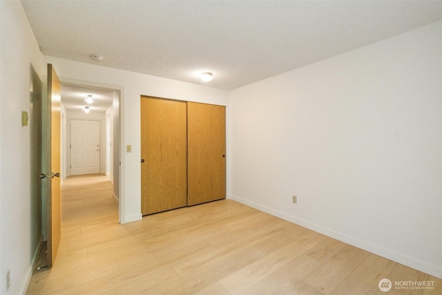 unfurnished bedroom with light wood finished floors, baseboards, and a closet
