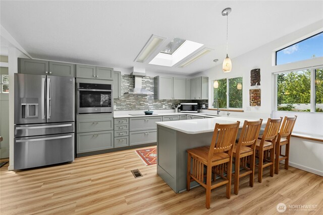 kitchen with stainless steel appliances, wall chimney range hood, a skylight, a peninsula, and tasteful backsplash