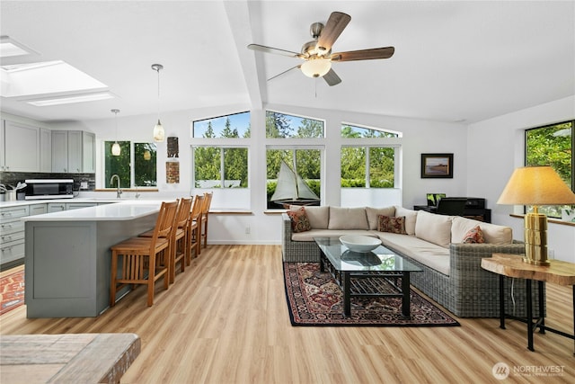 living area featuring light wood finished floors, ceiling fan, a skylight, and baseboards