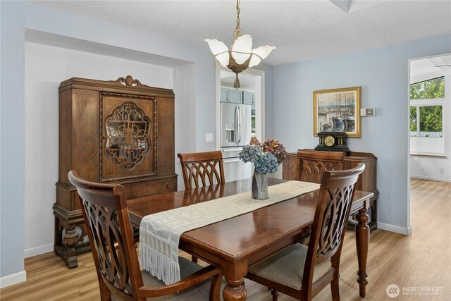 dining space with light wood-type flooring, a chandelier, baseboards, and a textured ceiling