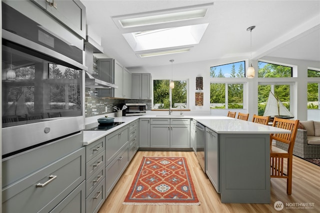kitchen with gray cabinets, appliances with stainless steel finishes, a skylight, a kitchen breakfast bar, and a peninsula