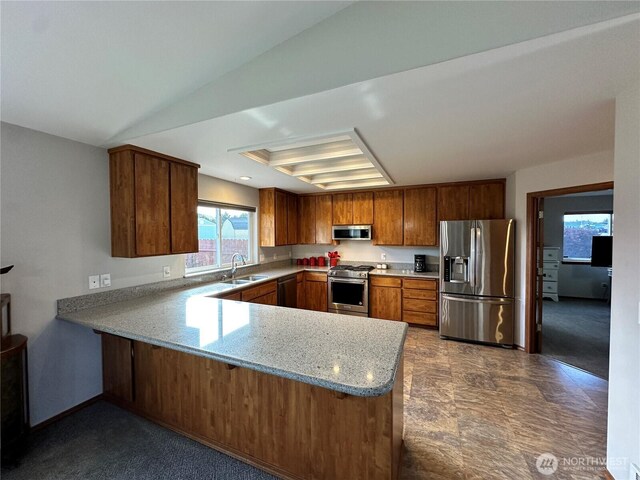 kitchen with stainless steel appliances, a sink, a peninsula, brown cabinetry, and light stone counters
