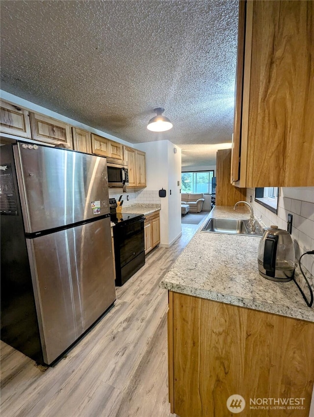 kitchen featuring stainless steel appliances, light wood-style floors, a sink, decorative backsplash, and light countertops
