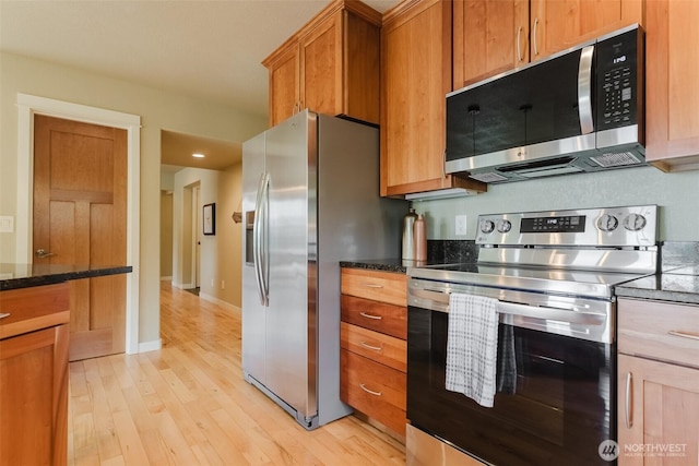 8070 Kispiox Rd, Blaine, WA 98230 - kitchen featuring appliances with stainless steel finishes, light wood-style floors, dark stone countertops, and brown cabinetry
