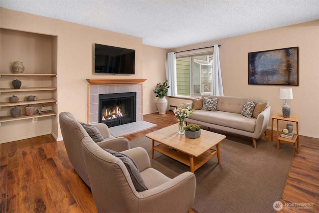 living room featuring a textured ceiling, a tile fireplace, wood finished floors, and a baseboard radiator