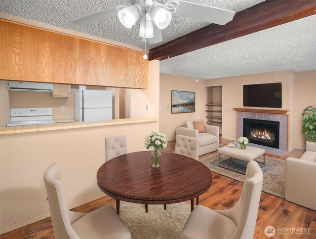 dining area with a textured ceiling, beam ceiling, a ceiling fan, wood finished floors, and a fireplace