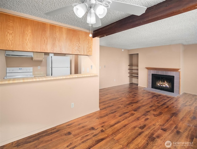 unfurnished living room with a textured ceiling, beamed ceiling, wood finished floors, a ceiling fan, and a tile fireplace
