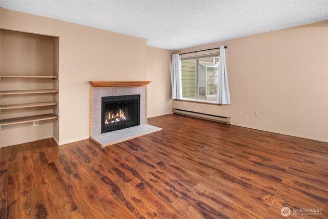 unfurnished living room featuring baseboard heating, wood finished floors, a fireplace, and a textured ceiling