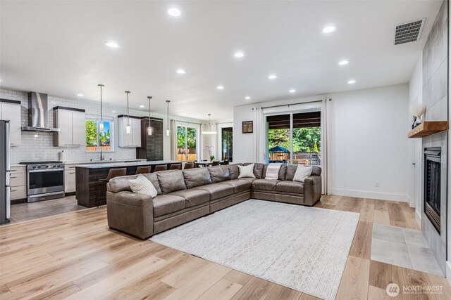living area featuring a large fireplace, recessed lighting, plenty of natural light, light wood-style floors, and baseboards