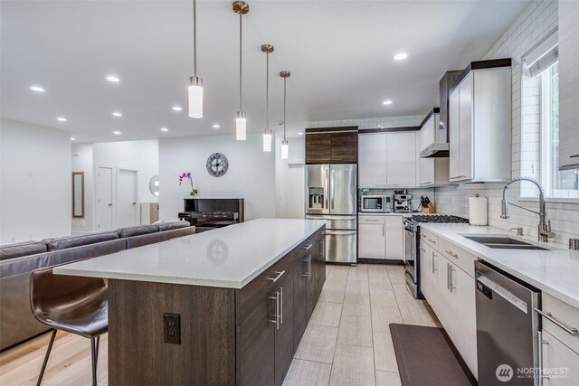 kitchen with appliances with stainless steel finishes, a sink, a center island, light countertops, and dark brown cabinetry