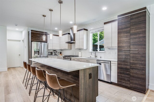 kitchen with stainless steel appliances, wall chimney exhaust hood, a sink, a center island, and decorative backsplash
