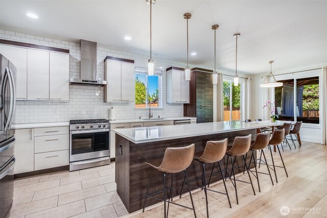 kitchen with appliances with stainless steel finishes, wall chimney exhaust hood, a breakfast bar, a sink, and plenty of natural light
