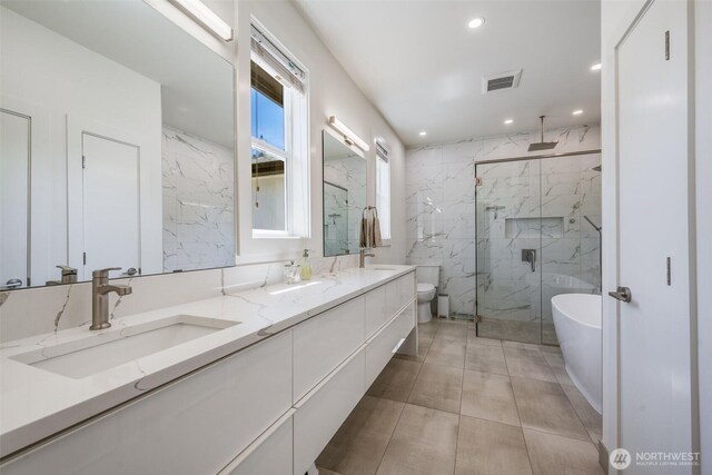 full bath featuring a marble finish shower, double vanity, a freestanding bath, recessed lighting, and toilet