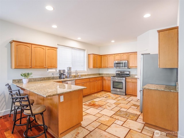 kitchen with stainless steel appliances, a peninsula, recessed lighting, a kitchen bar, and light stone countertops