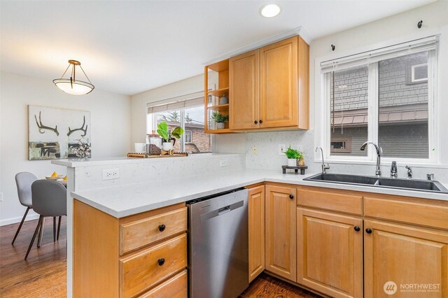 kitchen featuring stainless steel dishwasher, a sink, a peninsula, dark wood-style floors, and light countertops