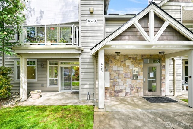 entrance to property featuring stone siding, a balcony, and a patio area