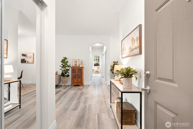 hallway featuring arched walkways, light wood-type flooring, baseboards, and ornamental molding
