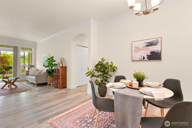 dining room featuring arched walkways, light wood-type flooring, crown molding, a chandelier, and baseboards