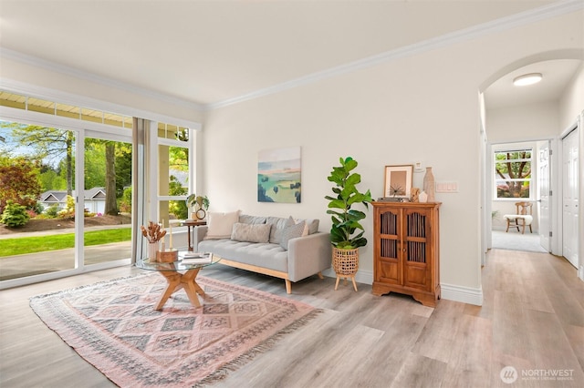 living area with arched walkways, light wood-type flooring, ornamental molding, and baseboards