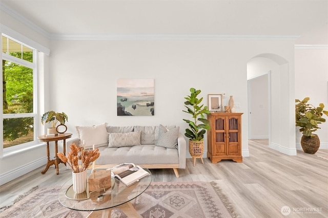 living area featuring arched walkways, ornamental molding, light wood-style floors, and baseboards