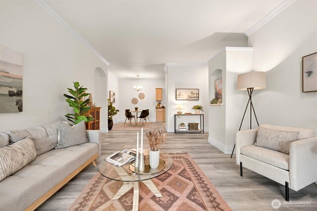 living room with crown molding, light wood finished floors, a chandelier, baseboards, and arched walkways