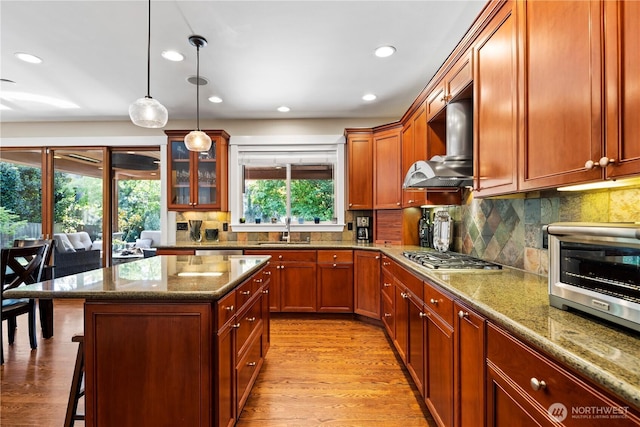 kitchen featuring stainless steel gas cooktop, a sink, a kitchen bar, wall chimney exhaust hood, and backsplash