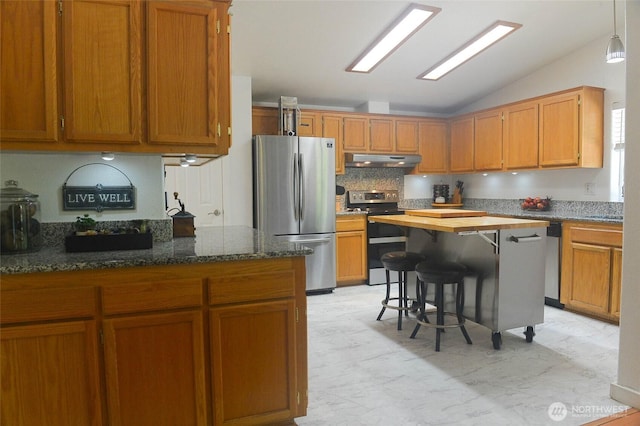 kitchen featuring appliances with stainless steel finishes, under cabinet range hood, vaulted ceiling, dark stone counters, and decorative backsplash