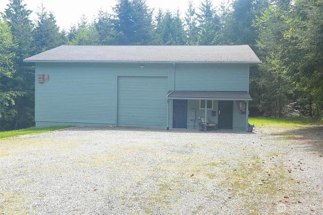 garage with gravel driveway and a view of trees
