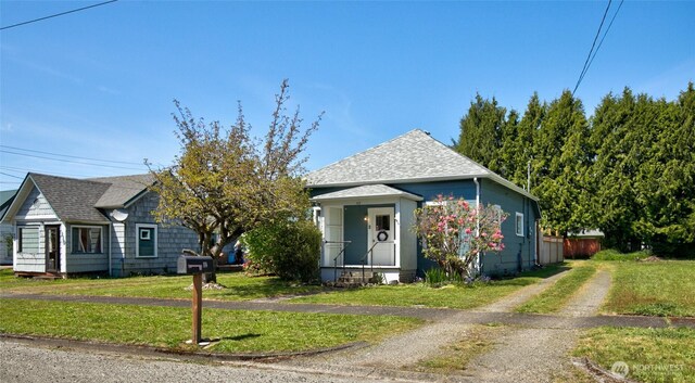 bungalow-style home with roof with shingles and a front lawn